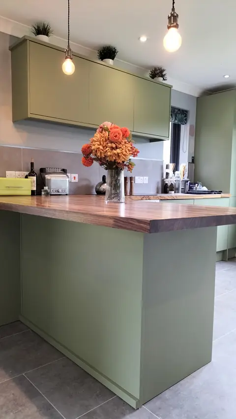 Sage green island with wooden worktop and pendant lights